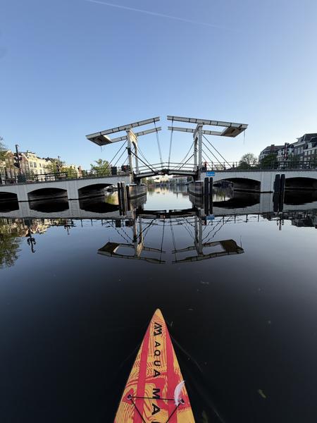 The photo captures a serene view from a paddleboard on the Amstel canal in Centrum, Amsterdam, looking towards a classic drawbridge